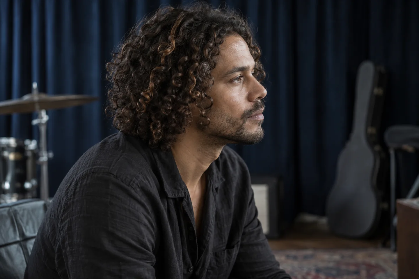 Adult man with dry dark curls and a few caramel strands in a rehearsal room with a navy curtain
