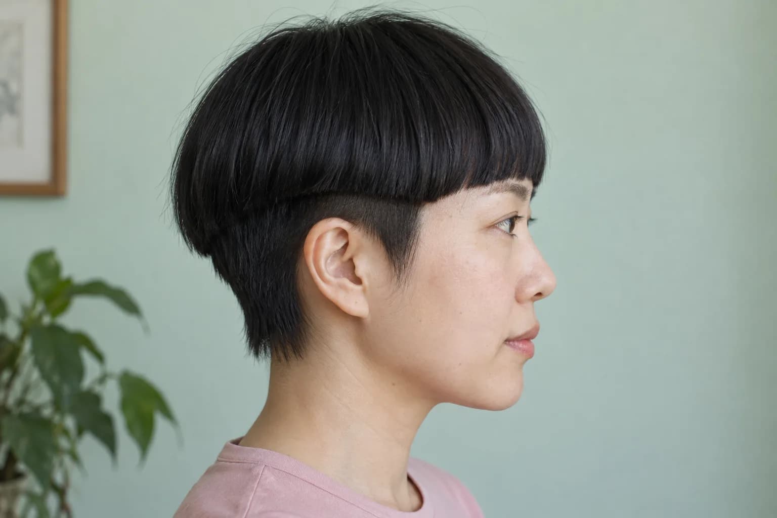 Femme adulte est-asiatique de profil avec une coupe au bol noire et des cheveux courts visibles sous le contour au-dessus de son oreille