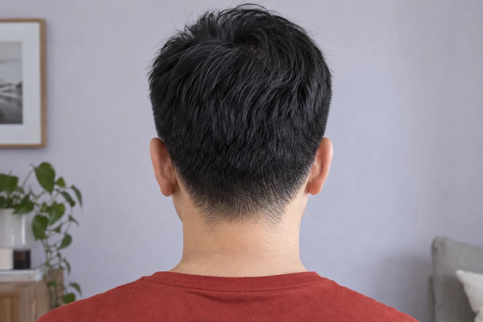 Rear view of an adult man with short black hair and a softly tapered natural neckline above a brick-red shirt